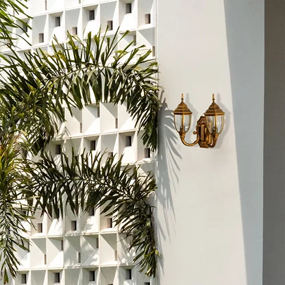 Double brass outdoor lantern with lights off fixed on a bright exterior wall featuring clear glass panels and antique brass finish for classic outdoor decor.