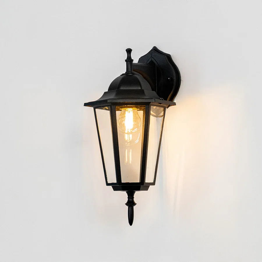 Black metal outdoor wall light on white background with clear glass shade for classic exterior decor.