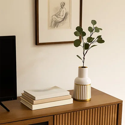 A white ceramic vase with gold detailing displayed on a wooden surface against a patterned backdrop adding a stylish accent to modern home decor.