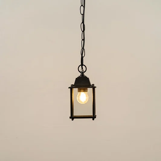 Black metal hanging outdoor lantern with square glass enclosure glowing on white background suitable for porch entrance and exterior decor lighting.