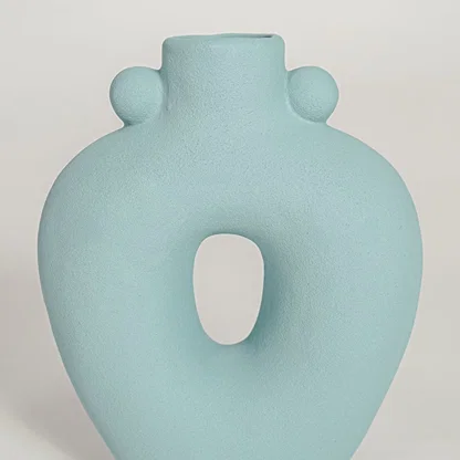 Closeup of matte light blue ceramic vase with curved hollow center ideal for elegant home decor shelf styling.