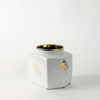 White ceramic decorative storage jar with gold bee artwork and gold rim for elegant shelf styling and home decor.