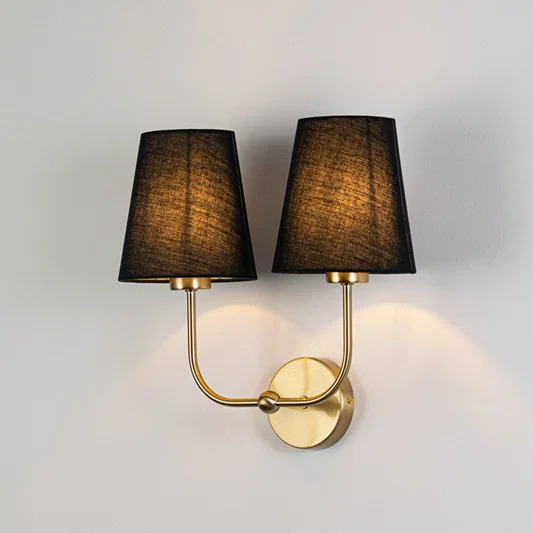 Elegant wall light in gold metal finish with dual dark fabric shades for bedroom or living decor lighting white background.