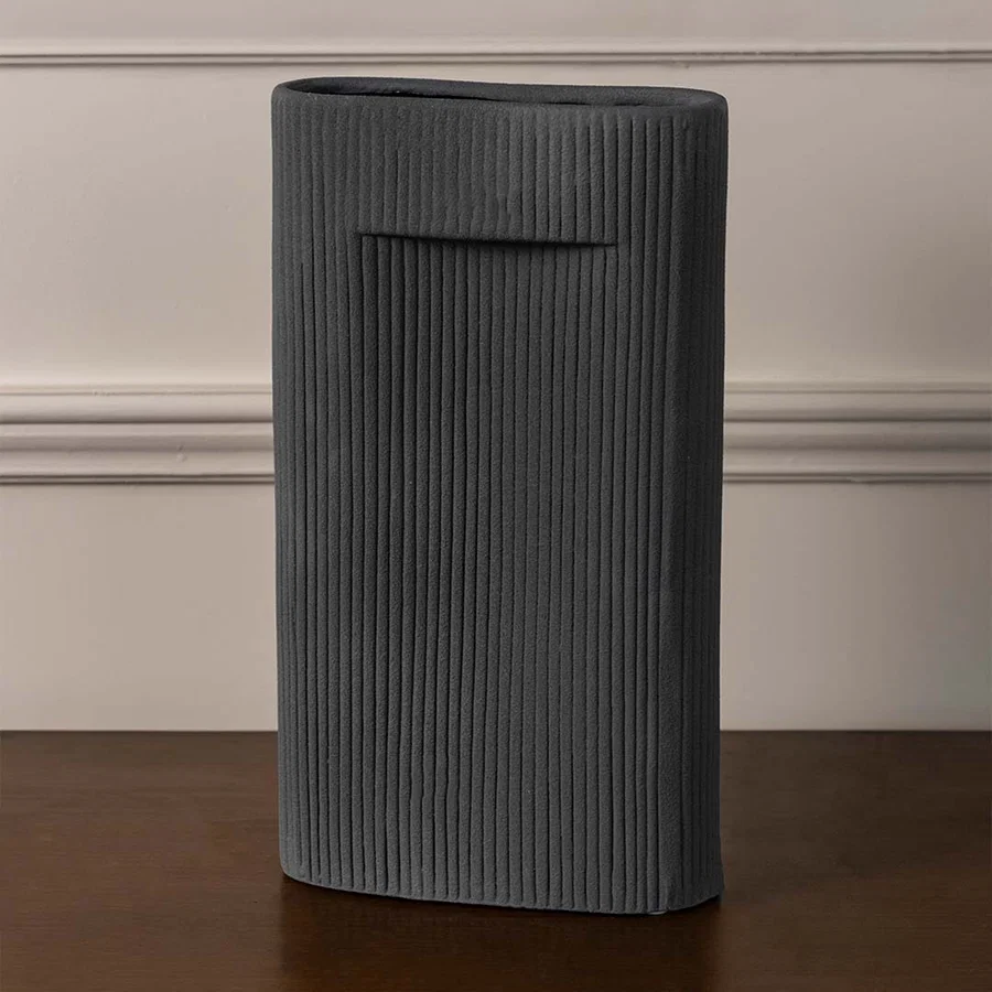 Ribbed grey ceramic cylindrical vase with vertical texture placed on white surface against neutral background enhancing modern minimal decor styling.