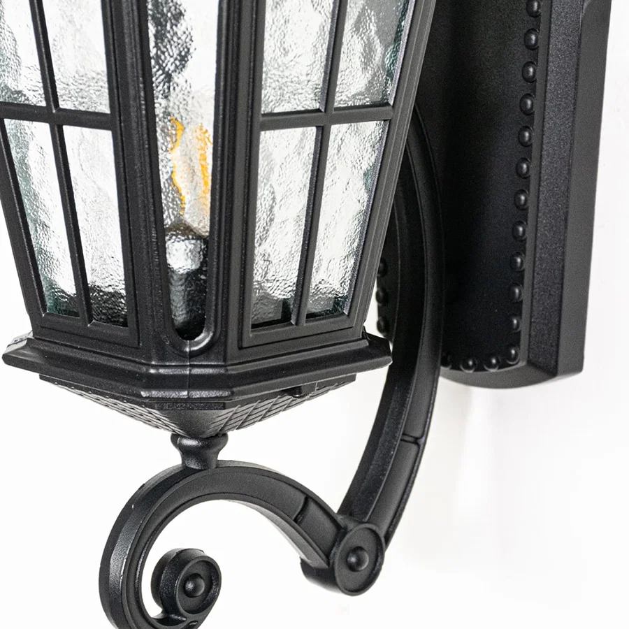 Closeup view of black metal wall lantern highlighting textured glass panels roof detailing and solid outdoor construction.