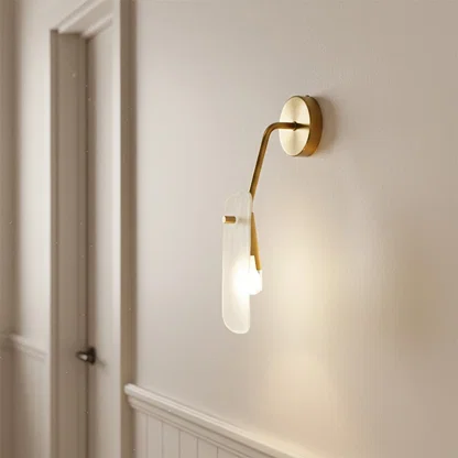 Luxury gold wall lamp with an artistic frosted glass panel diffuser illuminating a modern white hallway entry corner.