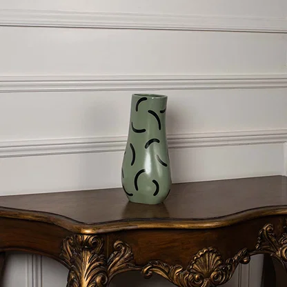 Matte green ceramic vase with black curved detailing shown on a white background highlighting its sculpted modern silhouette.