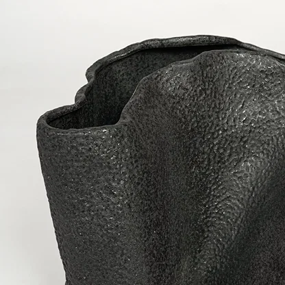 Detailed closeup of black metal decorative vase showcasing rough textured surface and abstract form.