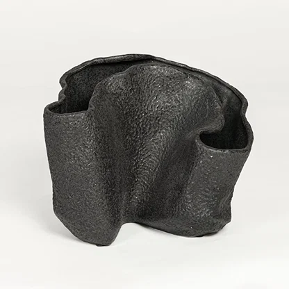 Black textured metal decorative vase with abstract curved design isolated on white background for contemporary interior decor.