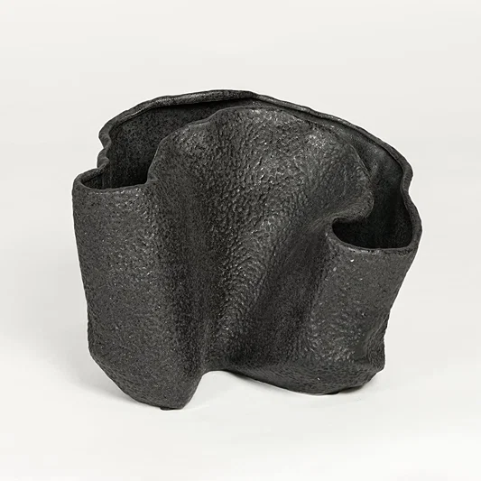 Black textured metal decorative vase with abstract curved design isolated on white background for contemporary interior decor.
