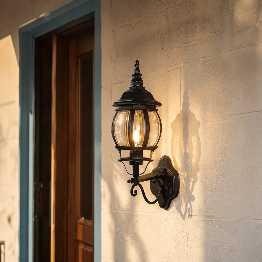 Vintage black metal scroll arm globe glass lantern wall sconce on exterior concrete stucco wall next to entryway door.