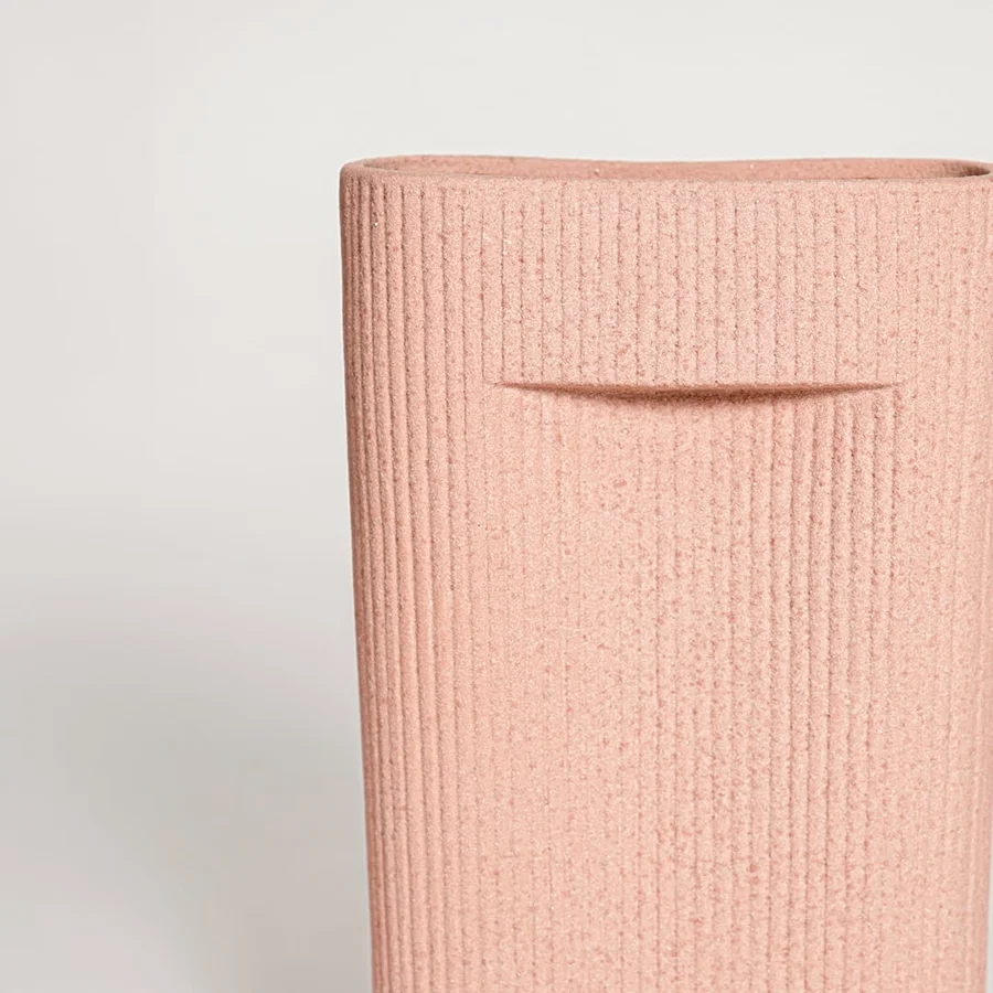 Closeup of matte peach ceramic vase with vertical lined texture ideal for elegant home decor shelf or side table styling.