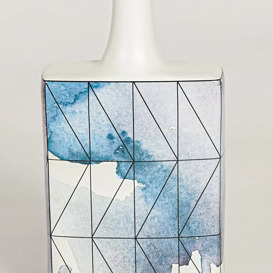 Closeup image of white ceramic artistic vase with blue geometric detailing for modern tabletop decor styling.