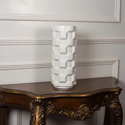 Lifestyle image of a white ceramic cylinder vase with interlocking block relief patterns on a vintage wood console table.