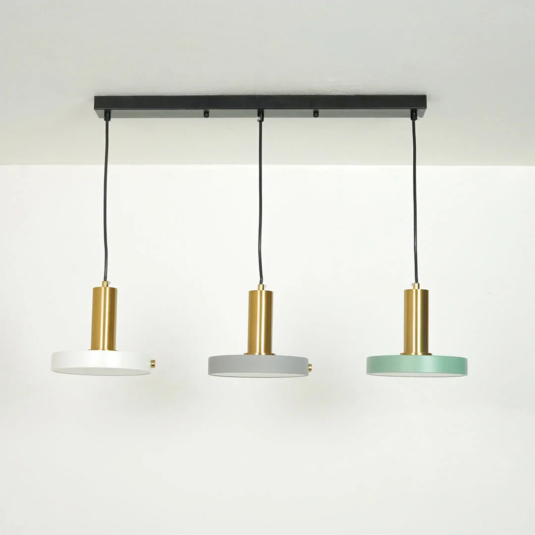 Three modern pendant lights hanging from a black ceiling bar. Each light has a cylindrical gold-toned metal shade, a black cord, and a round shade at the bottom in white, light gray, and mint green.