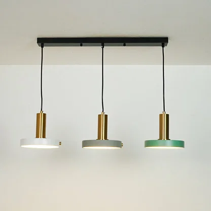 Three-light linear ceiling pendant fixture with a black horizontal bar, black cords, and three round shades in white, gray, and green with brushed gold centers, shown against a plain off-white wall.