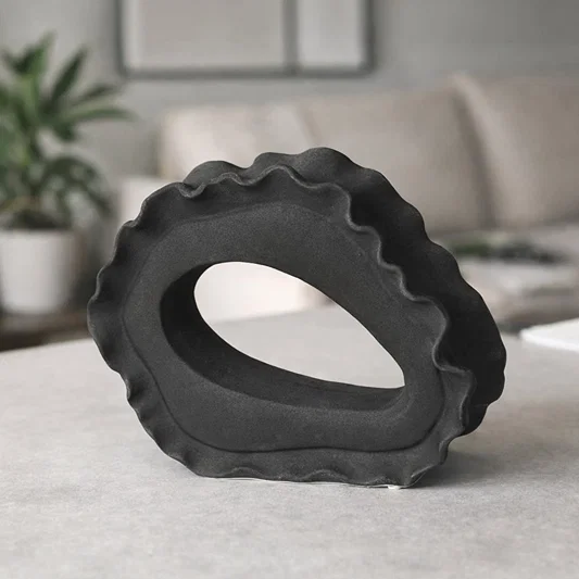 Dark grey ceramic abstract ring sculpture styled on console table for modern living room decor accent.
