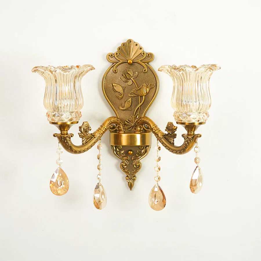 An ornate wall sconce with a gold-toned metal frame, two fluted clear glass shades, and hanging crystal teardrop pendants against a plain white background.