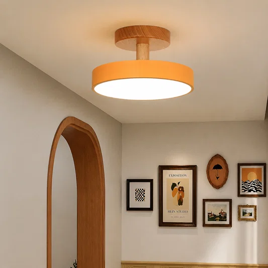 A modern ceiling light fixture with a warm orange drum shade and a natural wood ceiling mount, shown installed in a hallway with framed wall art and an arched doorway.