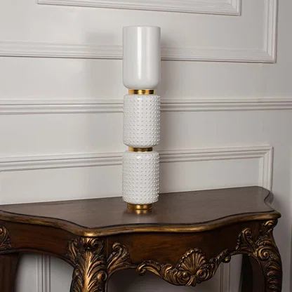 Glossy white tiered ceramic totem vase with gold structural rings displayed on a classic wooden console table for decor.