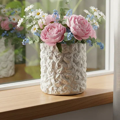 White ceramic decorative vase styled with pink flowers on a wooden table for elegant modern home decor settings.