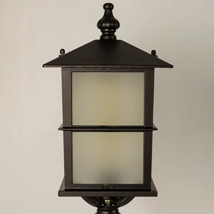 Closeup of a black outdoor pillar lamp showing glowing frosted glass and refined lantern edges designed for soft ambient garden and pathway lighting.