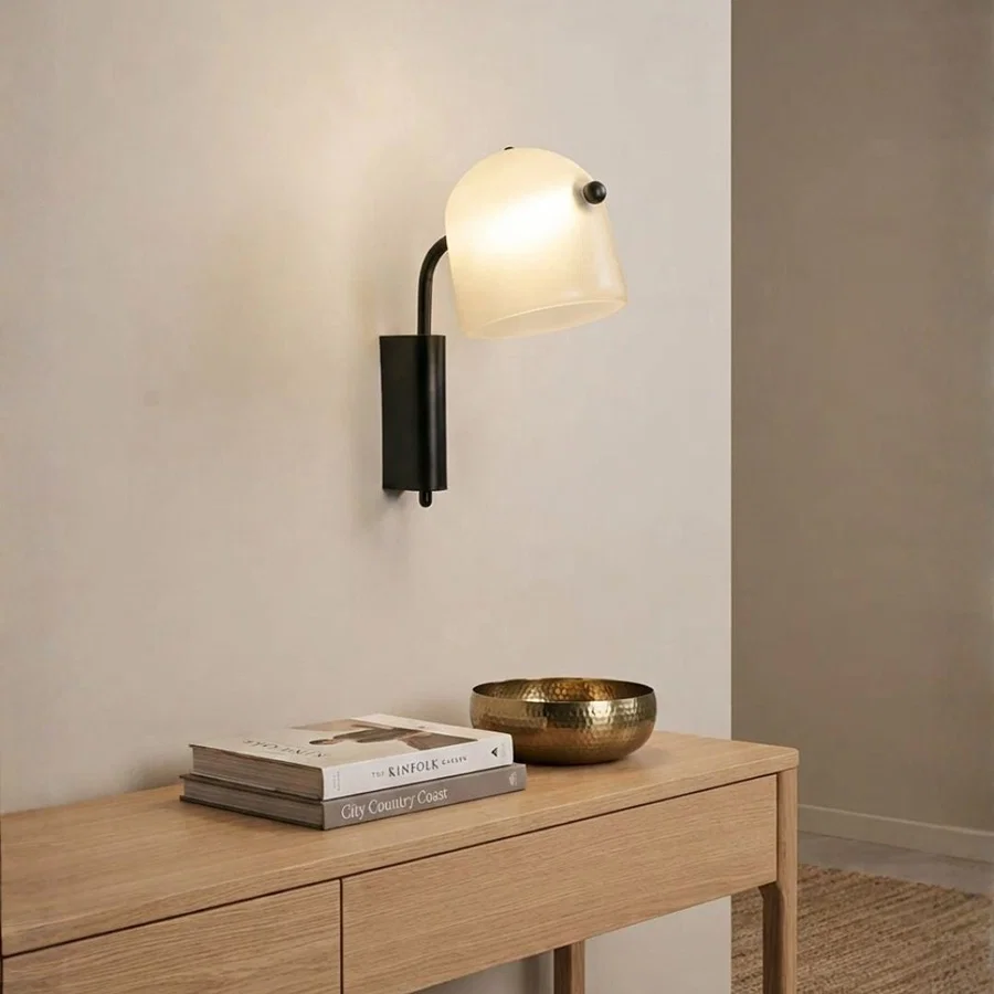 Minimalist black metal arm frosted glass dome wall sconce light over a wooden console table for modern entryway home decor.
