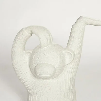 Close up of white monkey sculpture showing carved texture facial detail and raised arm design modern artistic decor piece.