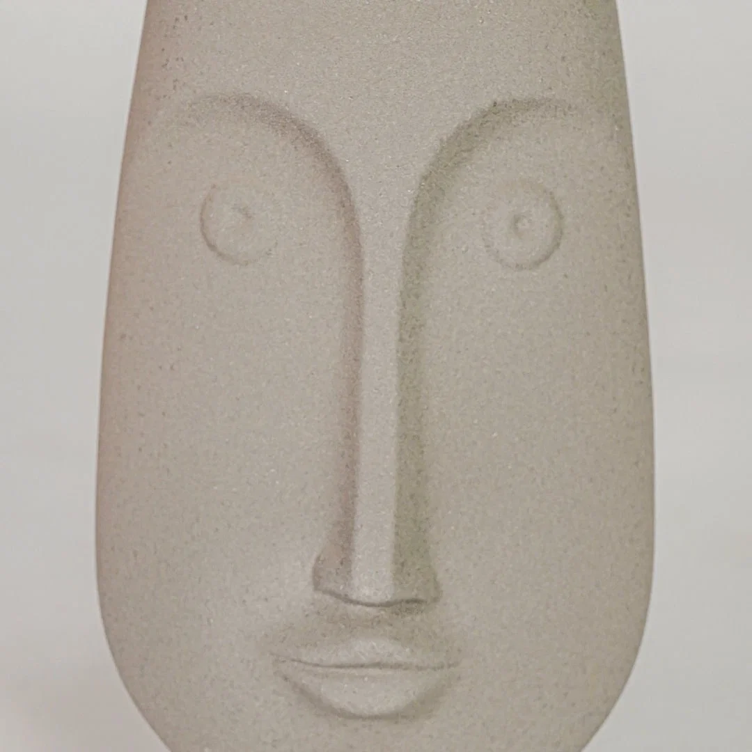 Closeup image of beige ceramic abstract face sculpture for modern shelf decor styling with matte finish display.