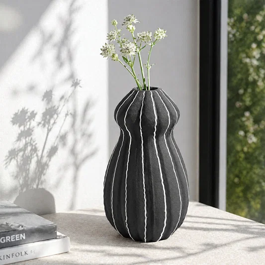 Black textured ceramic flower vase with white blooms placed on marble table for modern home decor styling.