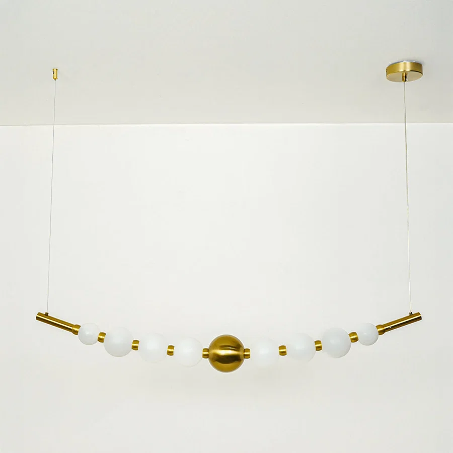 Stylish linear hanging light with multiple white glass globes and gold accents on neutral wall background perfect for modern dining or kitchen lighting.