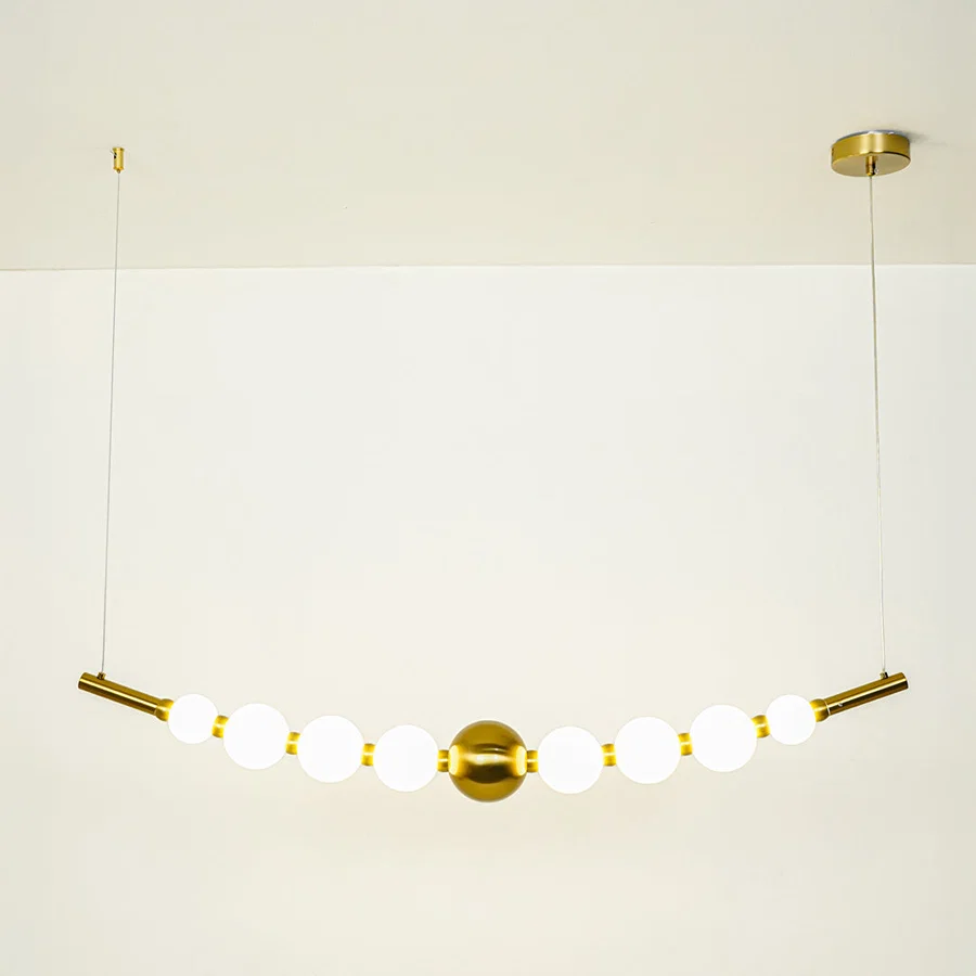 Minimal gold pendant light with white globe shades arranged in linear design on clean neutral background ideal for contemporary home lighting.