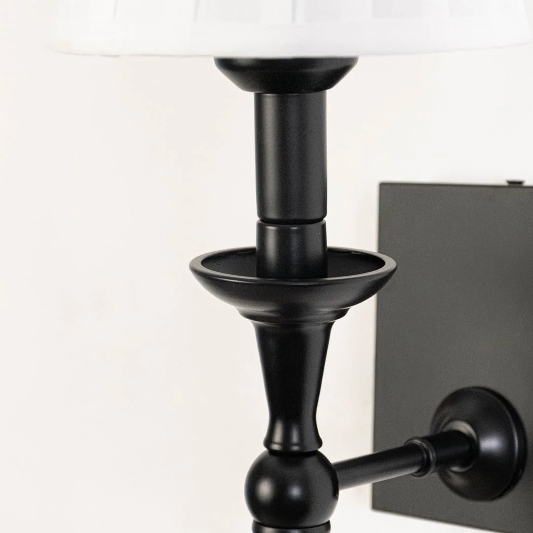 Closeup of black metal wall sconce with white pleated lampshade highlighting classic detailing and smooth finish.