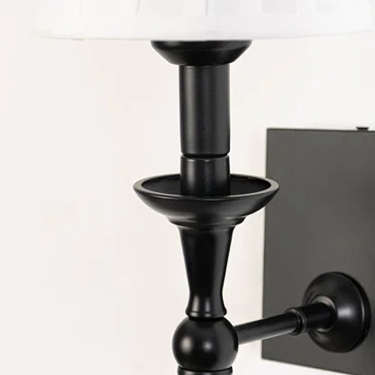 Closeup of black metal wall sconce with white pleated lampshade highlighting classic detailing and smooth finish.