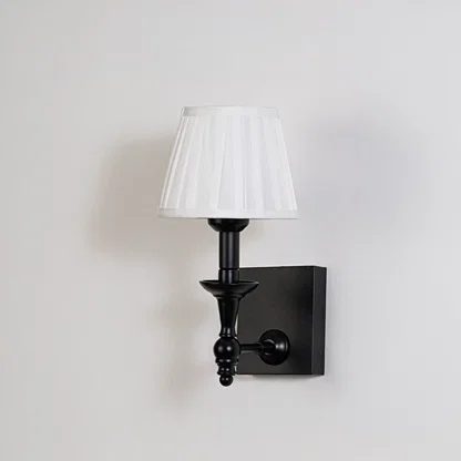 Black metal wall sconce with white pleated shade shown on a plain white background for accurate product clarity.