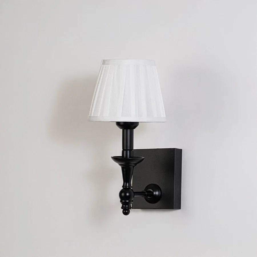 Black metal wall sconce with white pleated shade shown on a plain white background for accurate product clarity.
