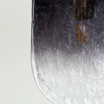 Textured glass pendant light with dark to clear gradient finish and gold bulb holder placed against neutral wall background closeup showcasing elegant lighting design.