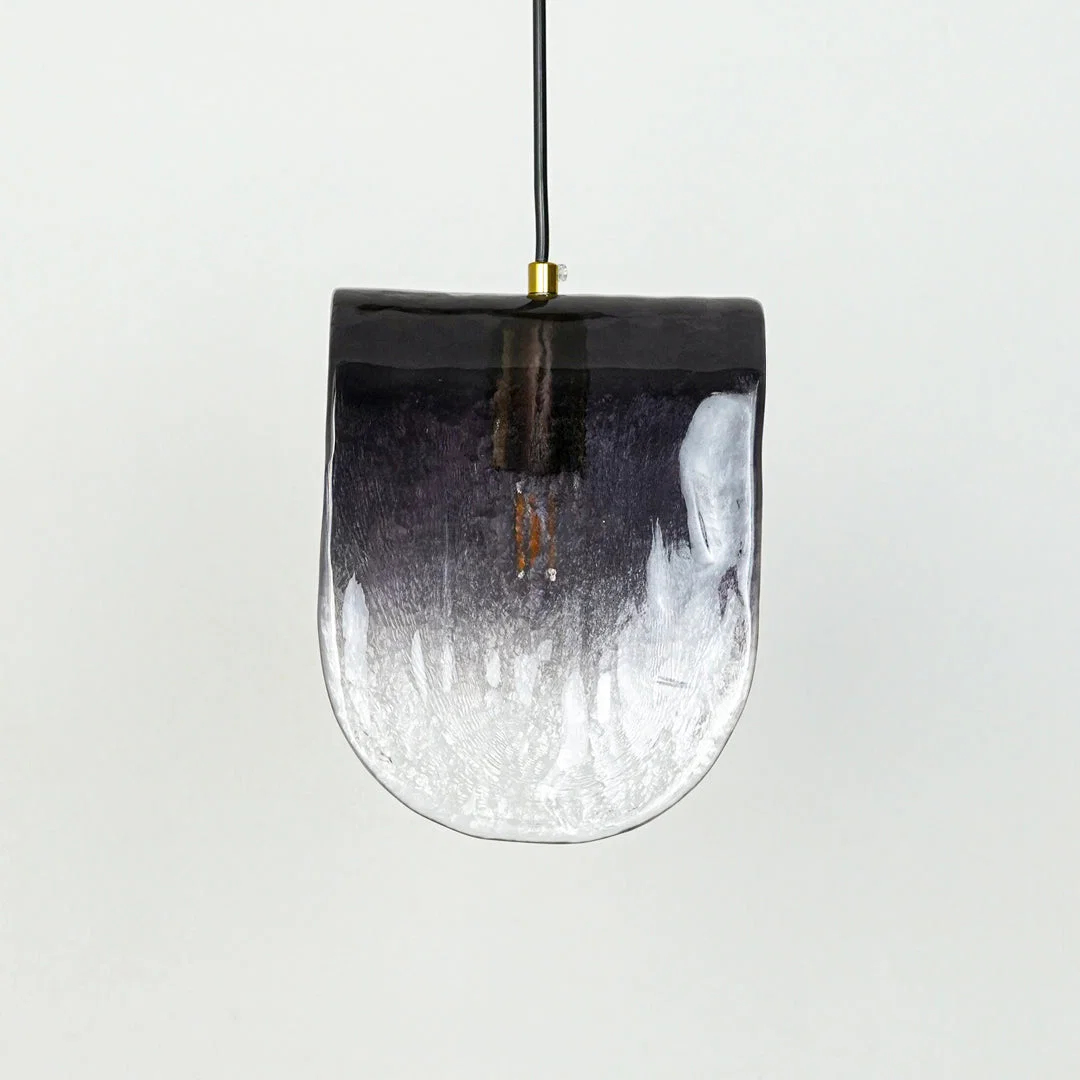 Gradient glass pendant light with curved shape and gold fixture hanging against neutral wall background enhancing contemporary decorative lighting aesthetic.