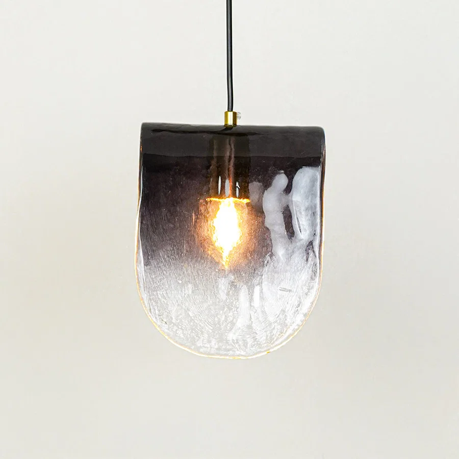 Frosted textured glass pendant light with glowing bulb and hanging cord placed against neutral wall background showcasing stylish modern lighting design.