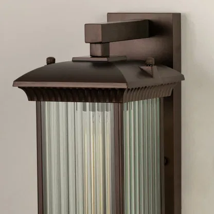 A closeup view of the bronze outdoor wall lantern showing the ribbed glass panels and warm glow highlighting the refined craftsmanship and elegant finish.