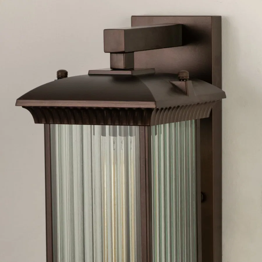 A closeup view of the bronze outdoor wall lantern showing the ribbed glass panels and warm glow highlighting the refined craftsmanship and elegant finish.