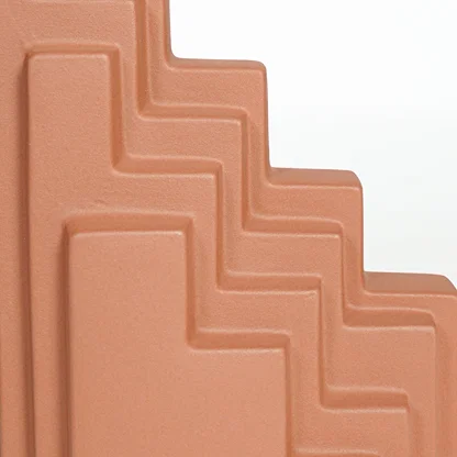 Close view of orange ceramic stepped decorative sculpture featuring angular layered design and refined matte finish.