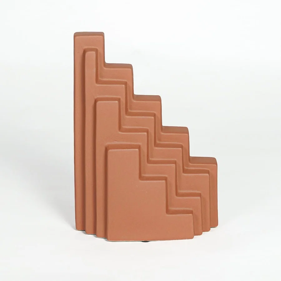 Orange ceramic stepped decorative sculpture with geometric layered design isolated on clean white background for contemporary decor display.