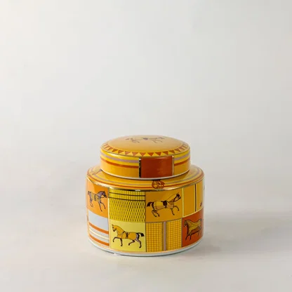 Decorative ceramic jar with lid featuring yellow and orange horse motif pattern on light off white background