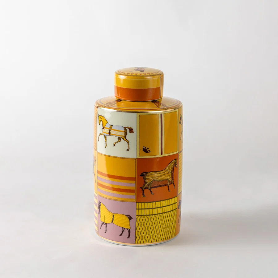 Amber ceramic decorative jar with vintage printed artwork and gold lid for elegant shelf styling and home decor.