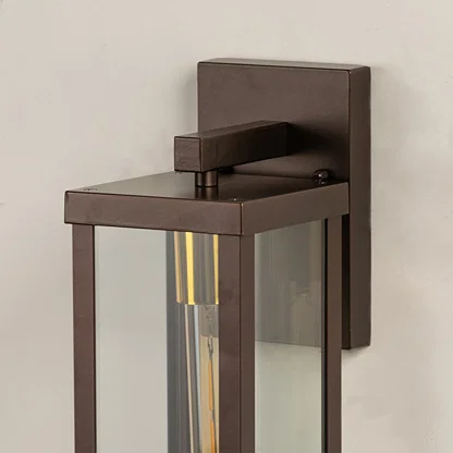 Closeup of bronze metal outdoor wall lantern showing warm tubular bulb inside clear glass frame perfect for modern porch patio and exterior Decor.