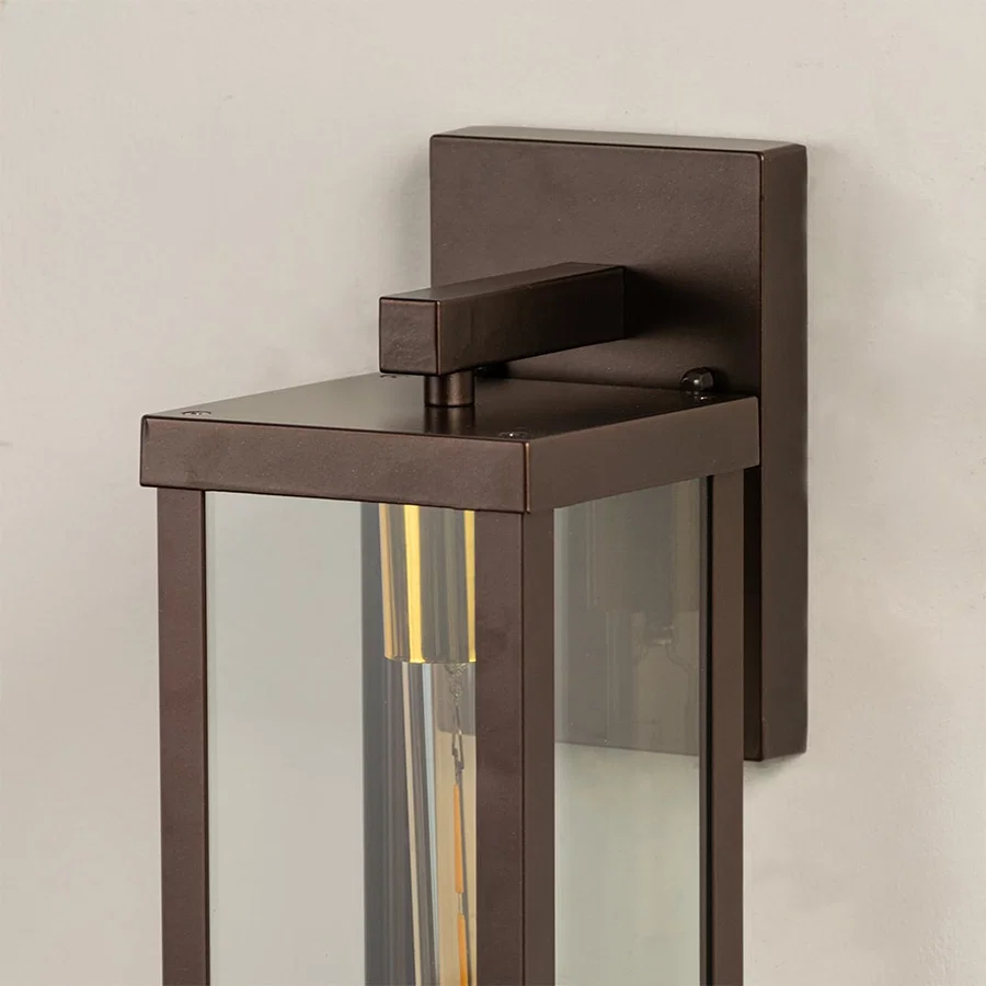 Closeup of bronze metal outdoor wall lantern showing warm tubular bulb inside clear glass frame perfect for modern porch patio and exterior Decor.