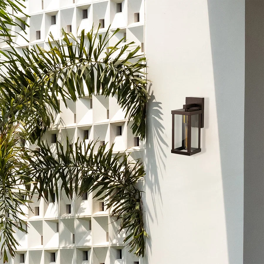 Bronze metal outdoor wall lantern light on mounted on a modern exterior wall with clear glass panels creating warm ambient lighting for patio porch and entry Decor.