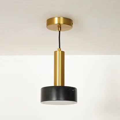 A modern pendant light fixture with a brushed gold metal cylinder, a black cylindrical shade, and a gold ceiling canopy, shown hanging against a white wall and ceiling.