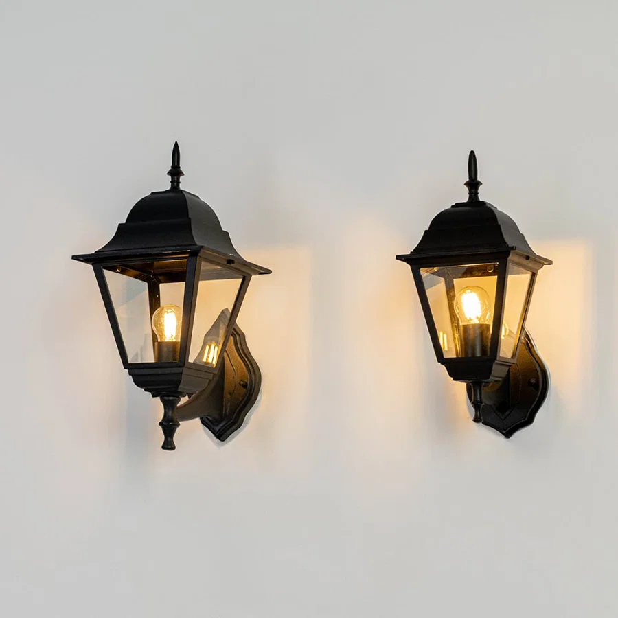 Set of elegant black outdoor wall lights illuminated on white background showcasing classic lantern shape and bright bulbs.